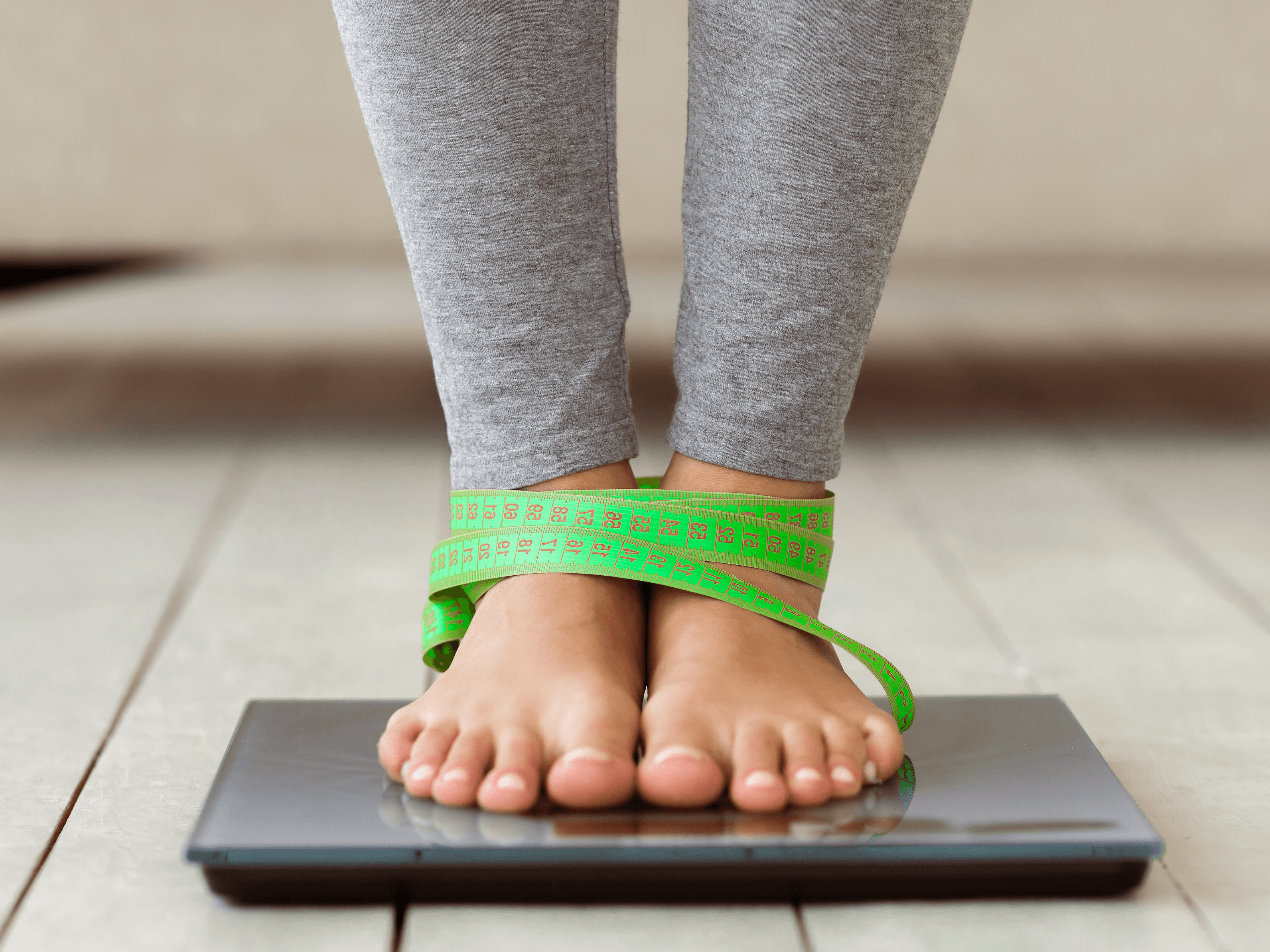 Pessoa em balança com fita métrica nos pés, simbolizando controle de peso e metabolismo.