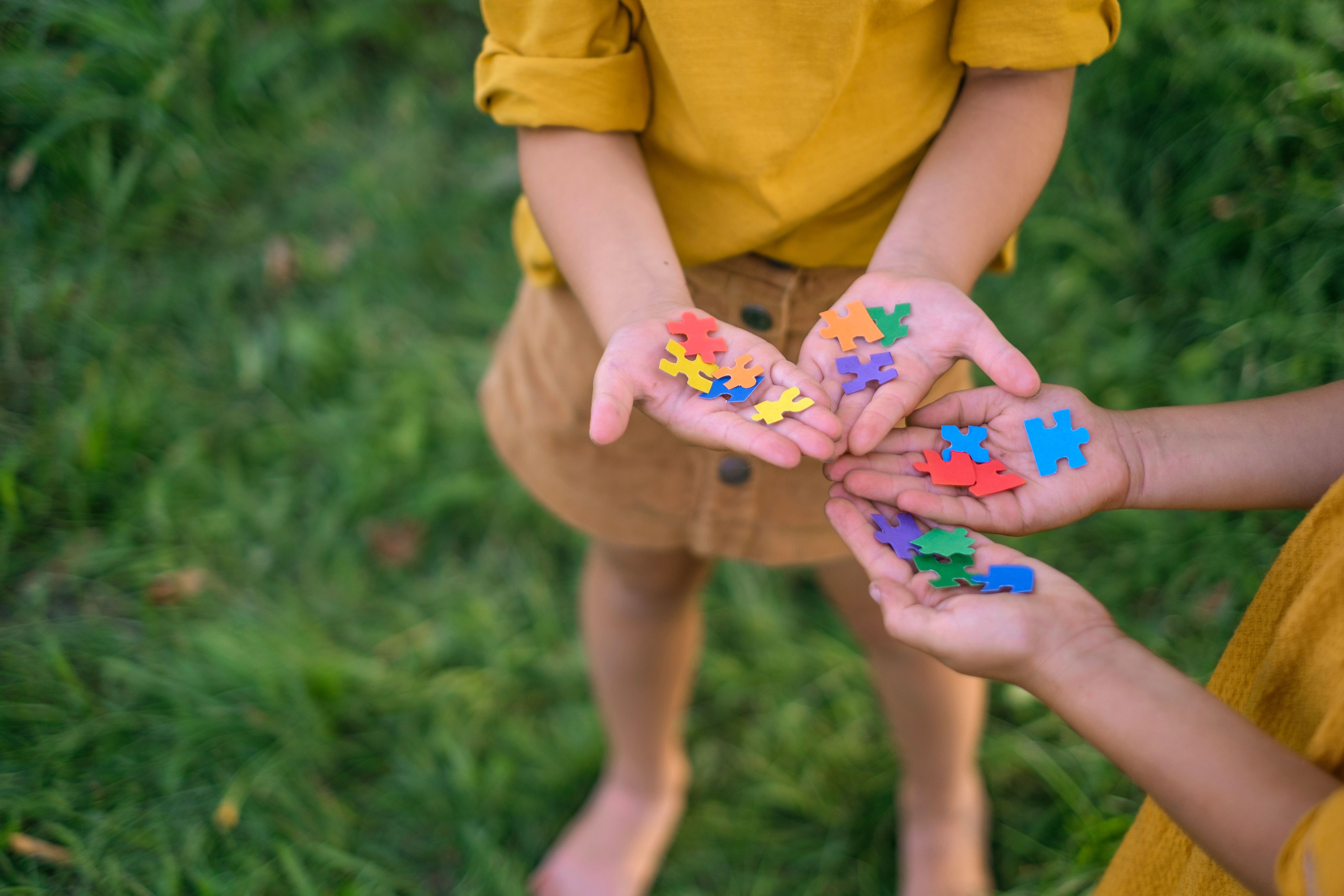 Duas crianças vestindo roupas amarelas seguram peças coloridas de um quebra-cabeça, representando o dia do autismo. 