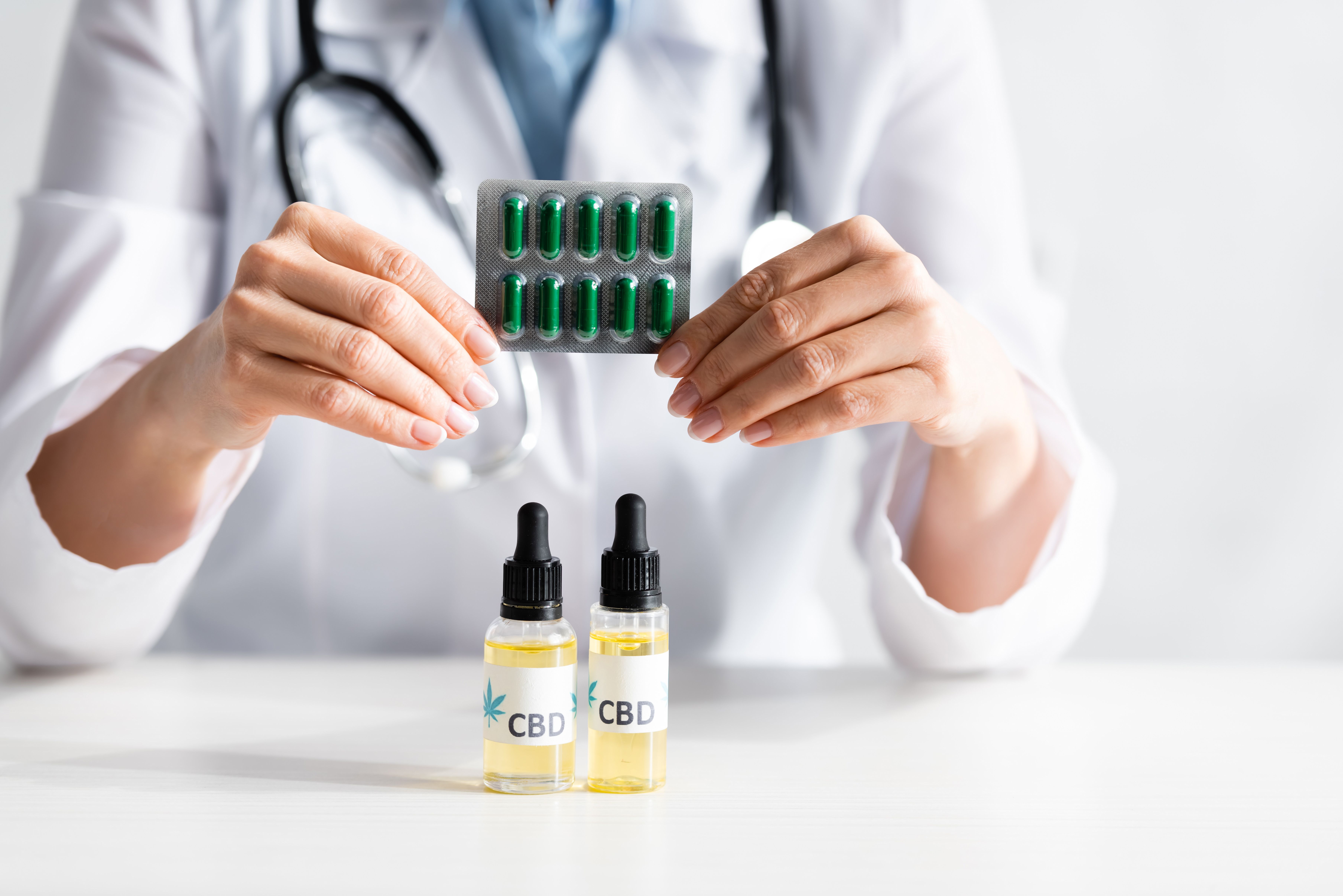  Profissional de saúde exibe cápsulas de ibuprofeno enquanto dois frascos de óleo de canabidiol (CBD) estão posicionados na frente. 