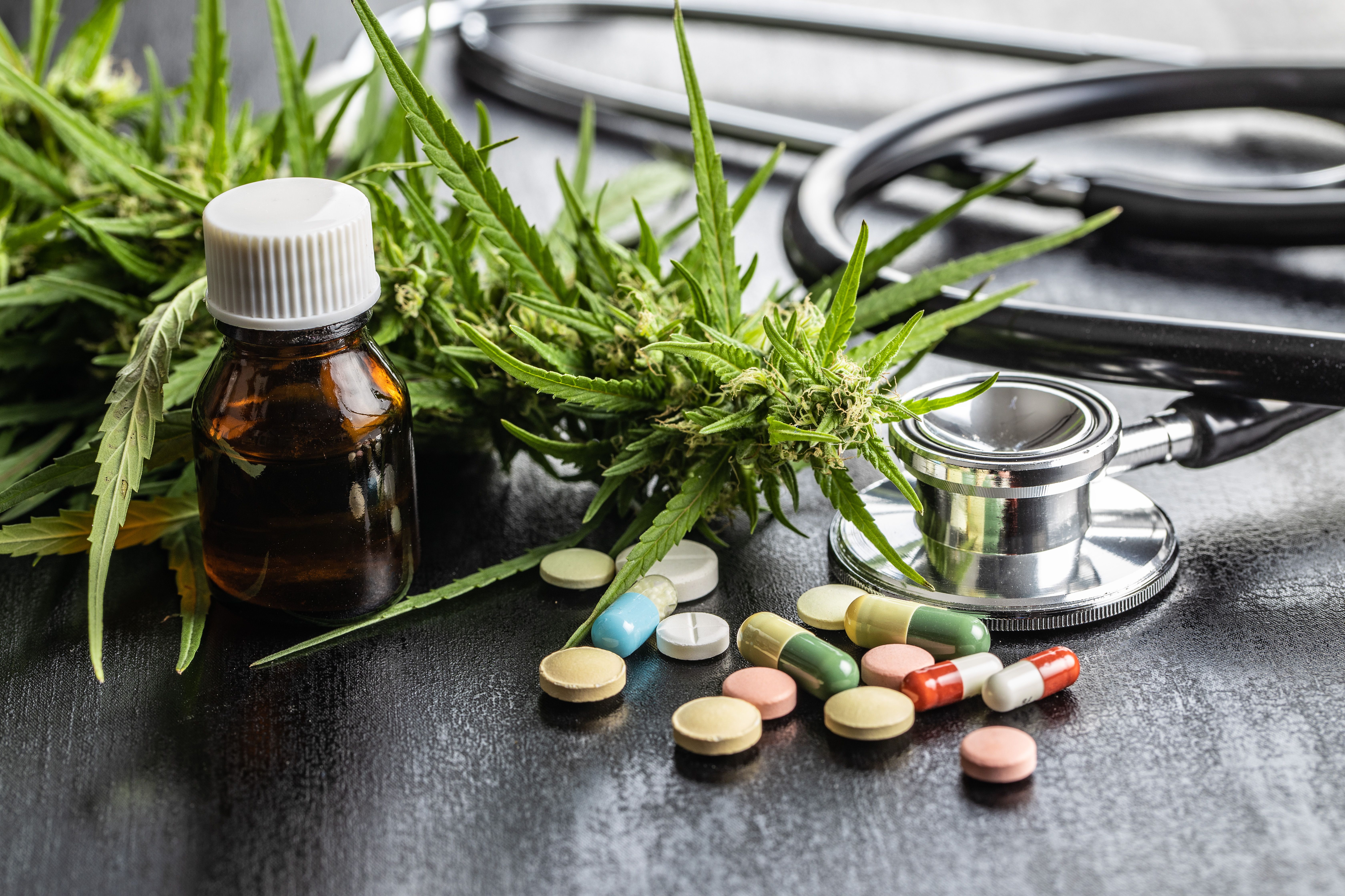 Composição mostrando plantas de cannabis medicinal, óleo de CBD em frasco âmbar, estetoscópio médico e diversos medicamentos sobre superfície.