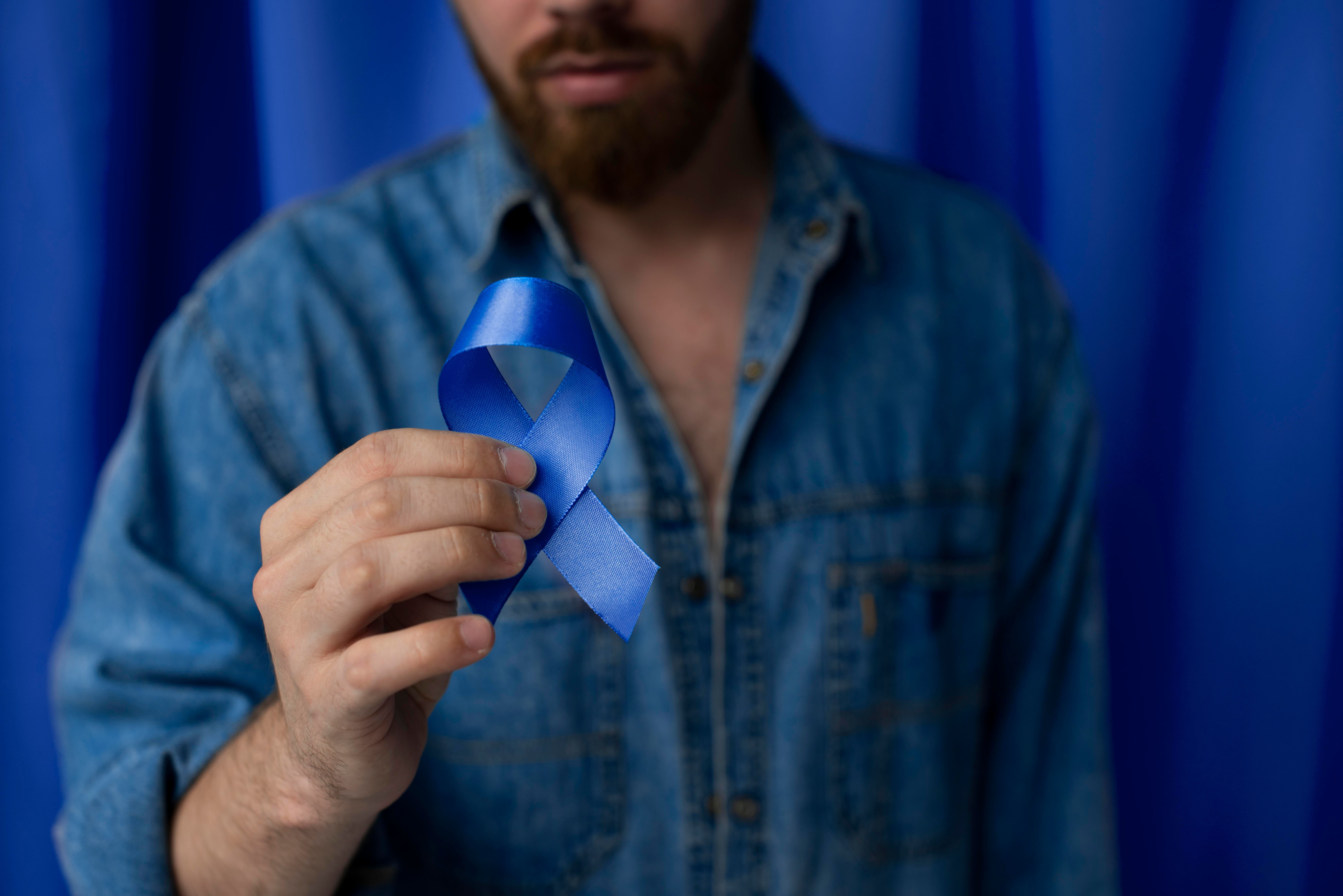 Homem segurando um laço azul, símbolo da campanha Março Azul Marinho de conscientização sobre o câncer de intestino